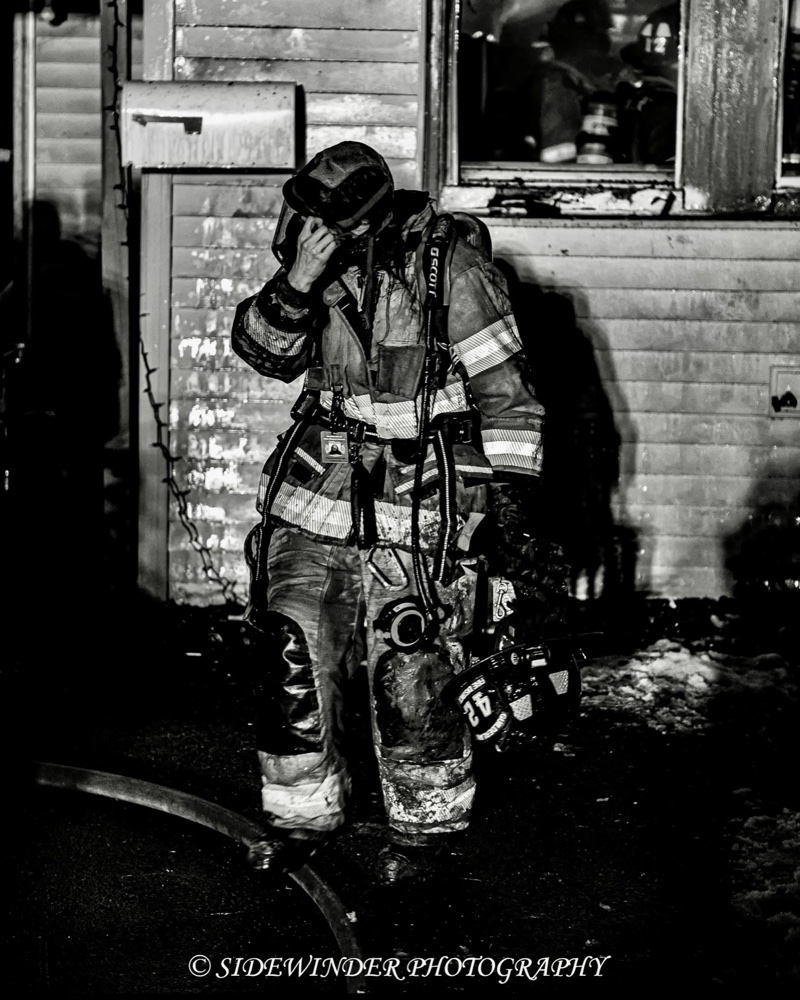Elizabeth MacDonald in turnout gear walking out from a fire-damaged house