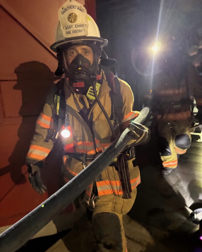 Mike Dempsey in an assistant chief's helmet and SCBA mask, advancing a handline at a drill
